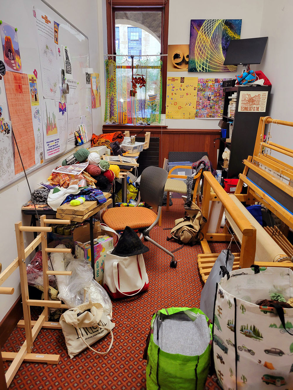 Quinn's very messy office with books and textile things everywhere, including several looms