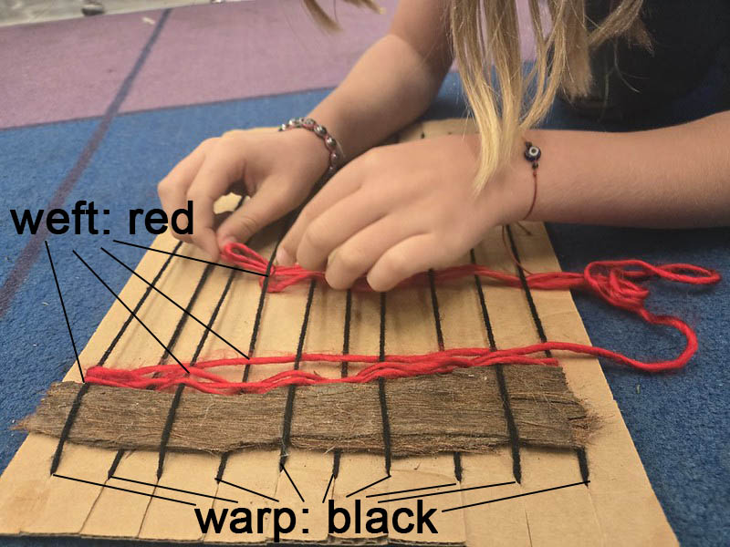 Weaving red weft yarns into black warp yarns on a cardboard loom